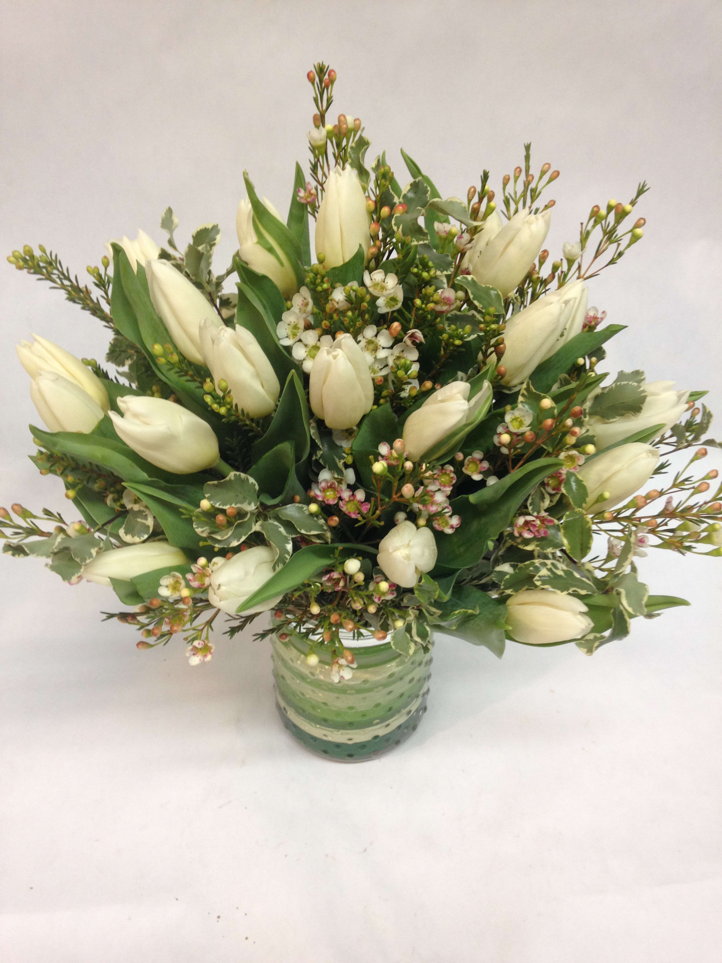 White tulips arranged in a green glass vase with small filler flowers