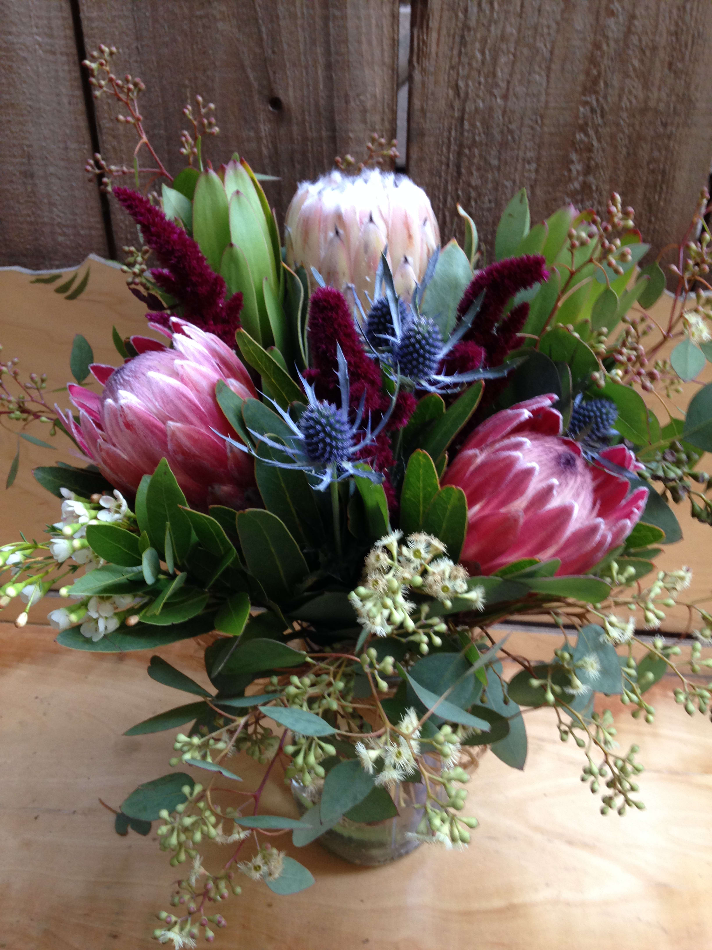 Bouquet of pink protea and burgundy filler flowers in a glass vase