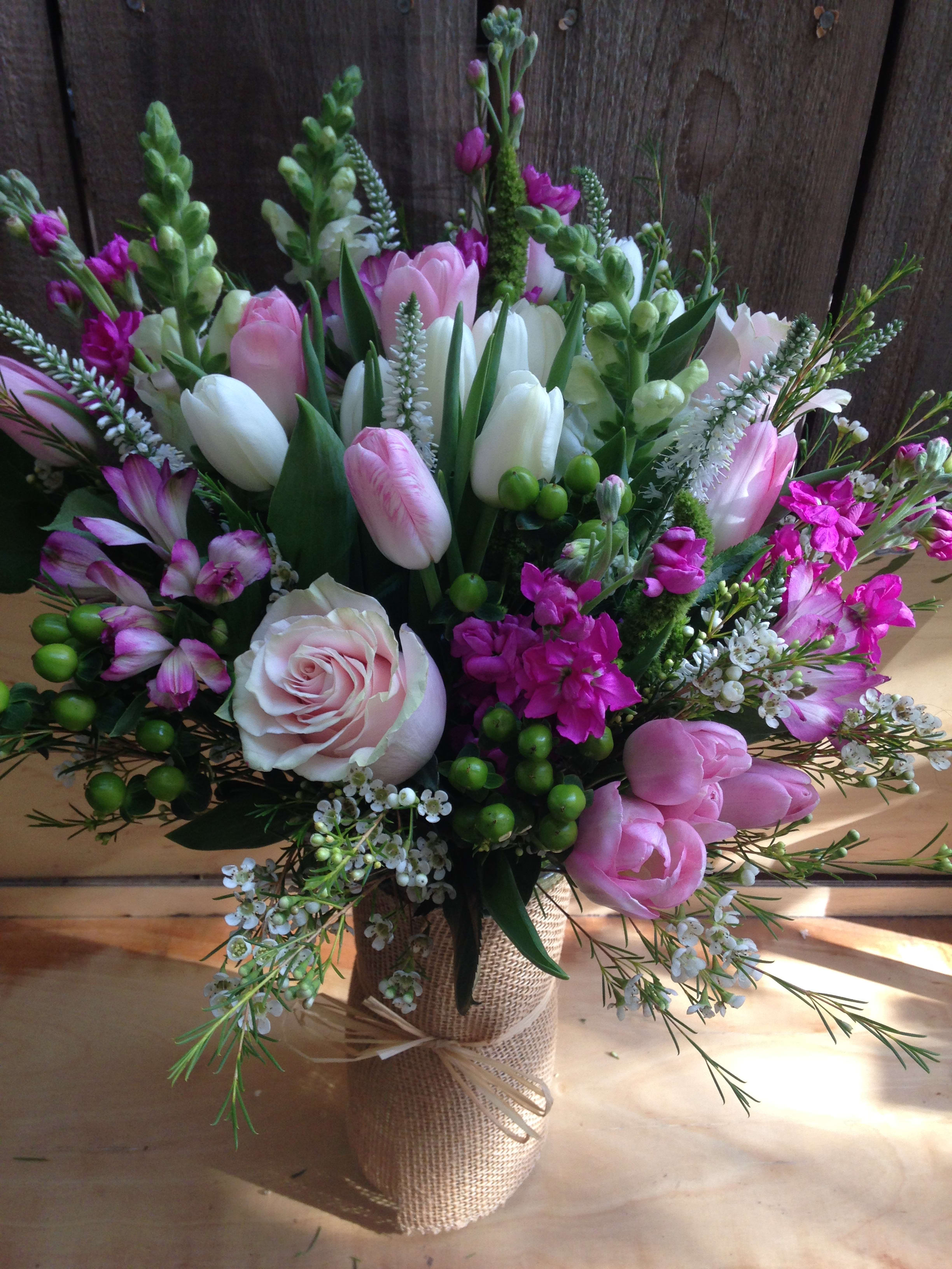 Bouquet of pink and white tulips, roses, and purple flowers in a burlap-wrapped vase