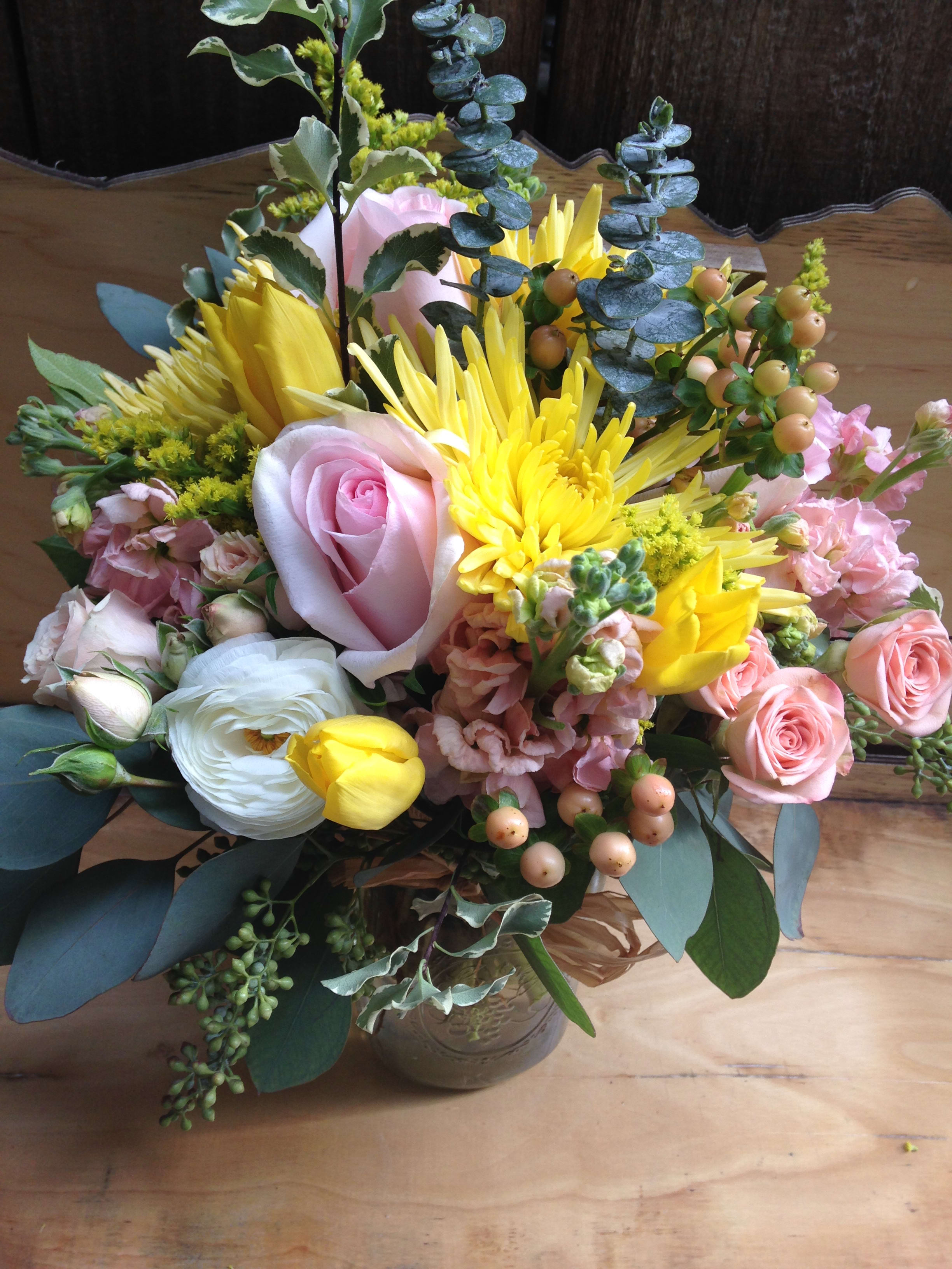 Mixed bouquet of pink roses, yellow blooms, and white flowers in a glass vase