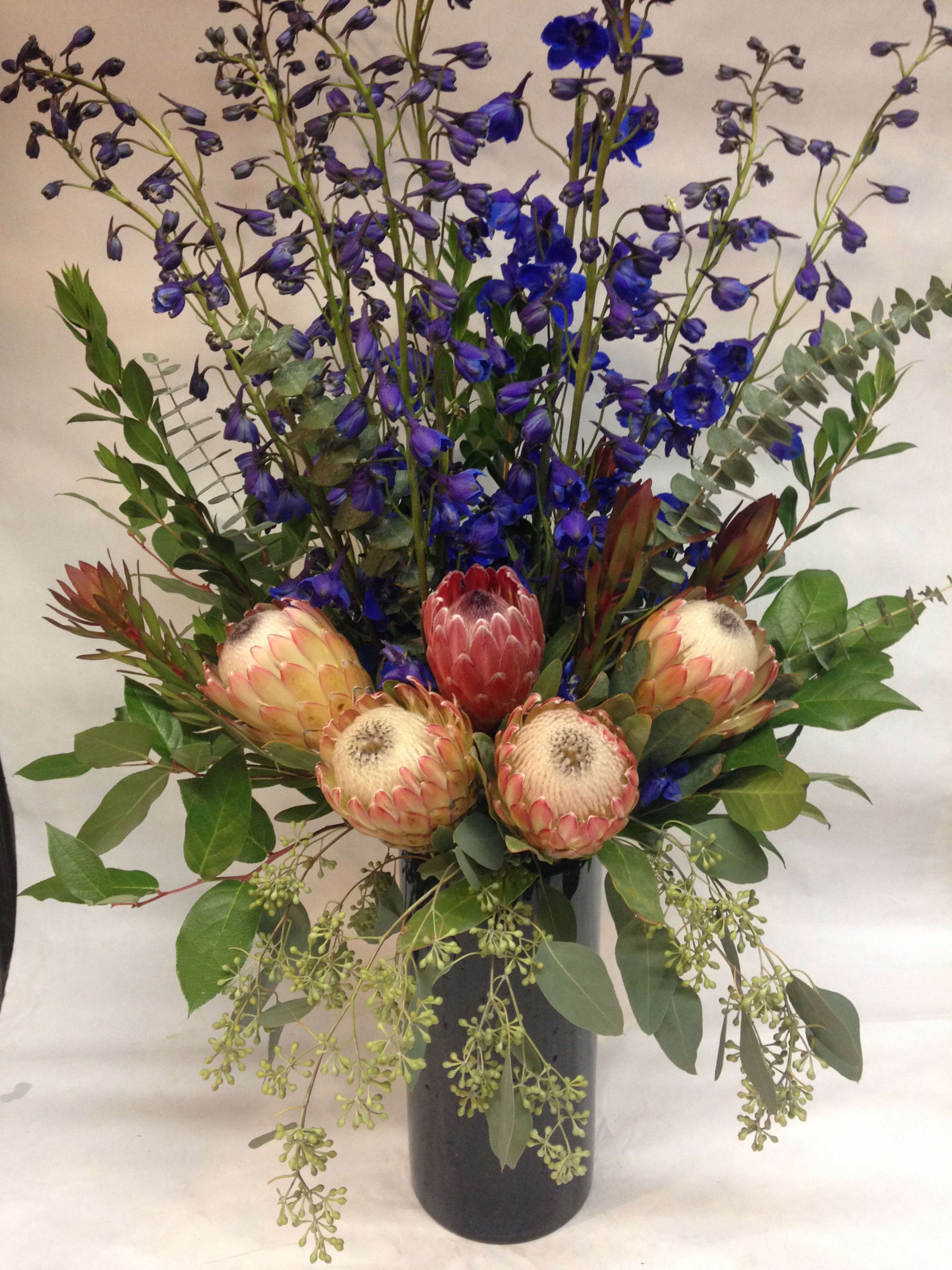 Tall bouquet with blue delphinium and pink protea in a black vase
