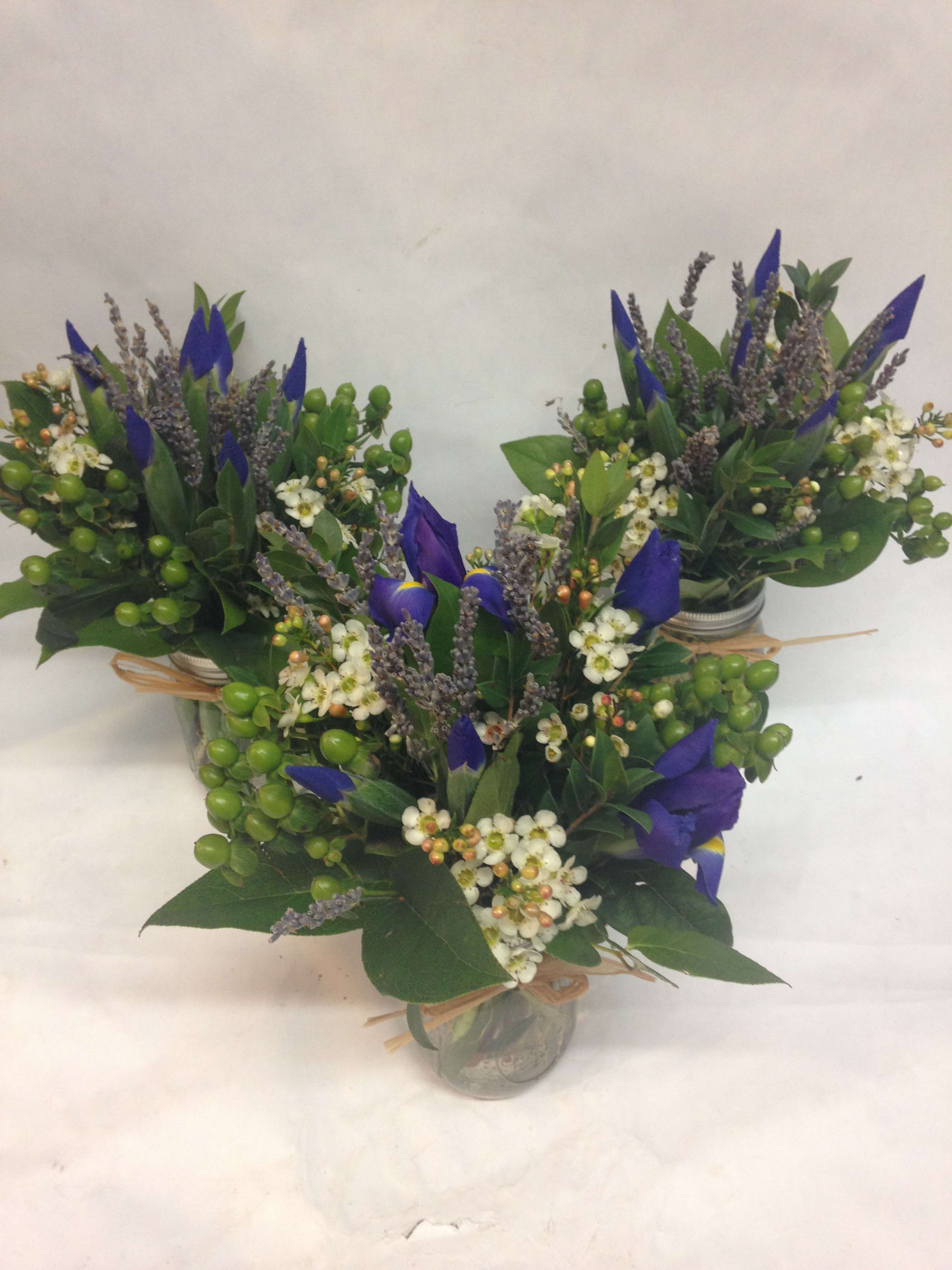 Three small blue-and-white floral arrangements in glass jars