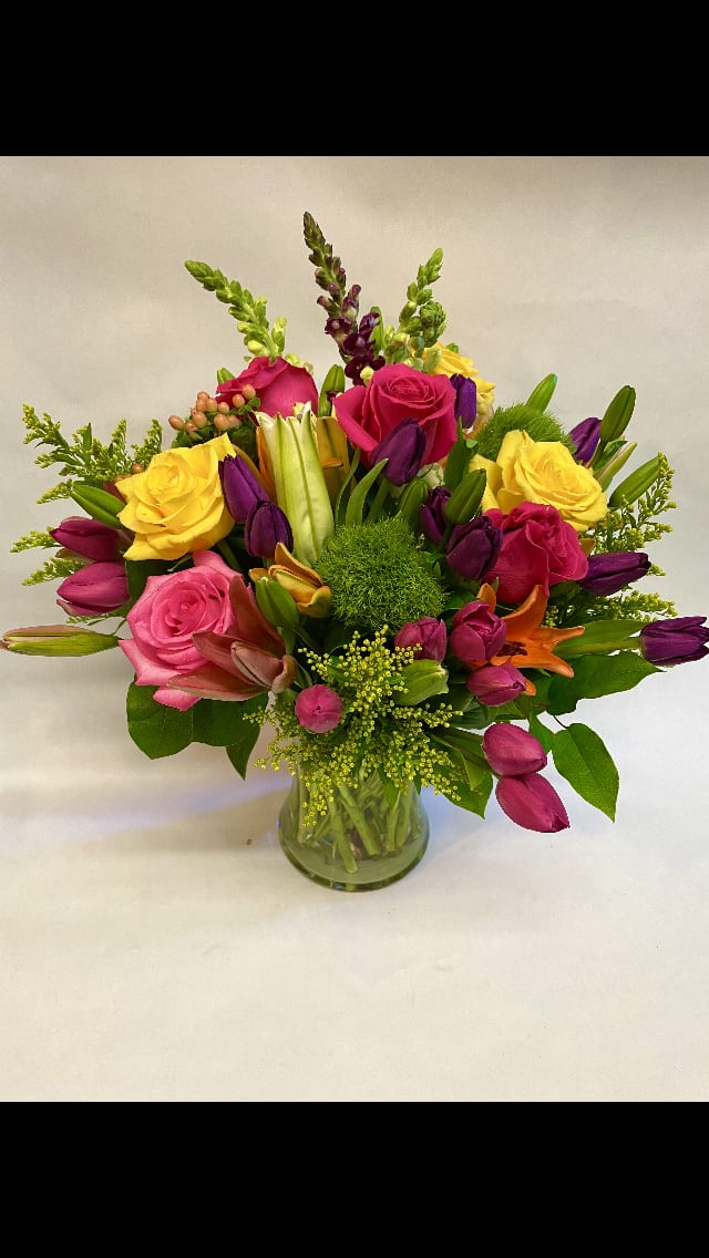 Mixed bouquet of roses, tulips, lilies, and snapdragons in a glass vase