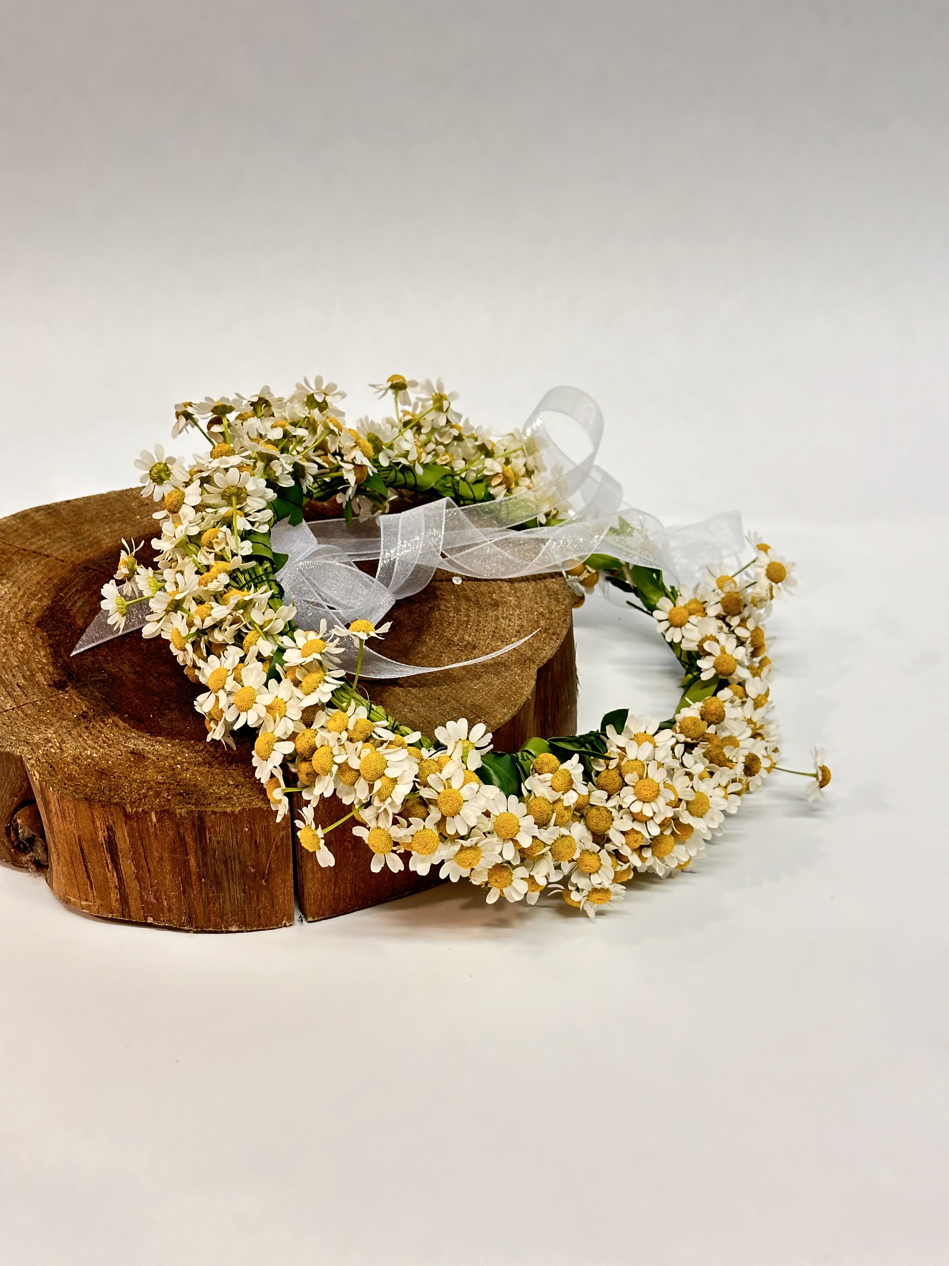 Daisy flower crown with white ribbon on a wooden stand