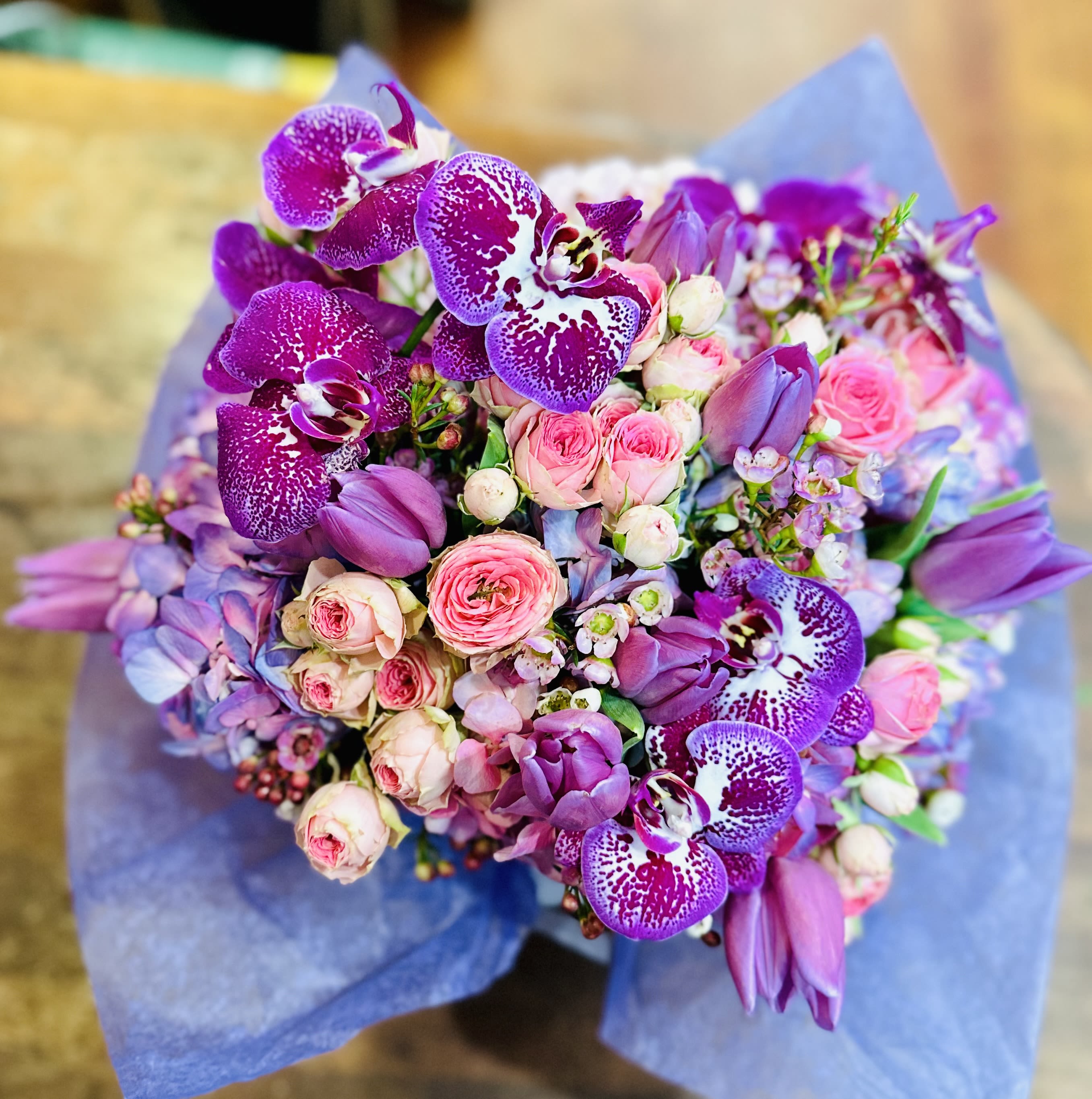 Bouquet of purple orchids and pink roses wrapped in blue paper