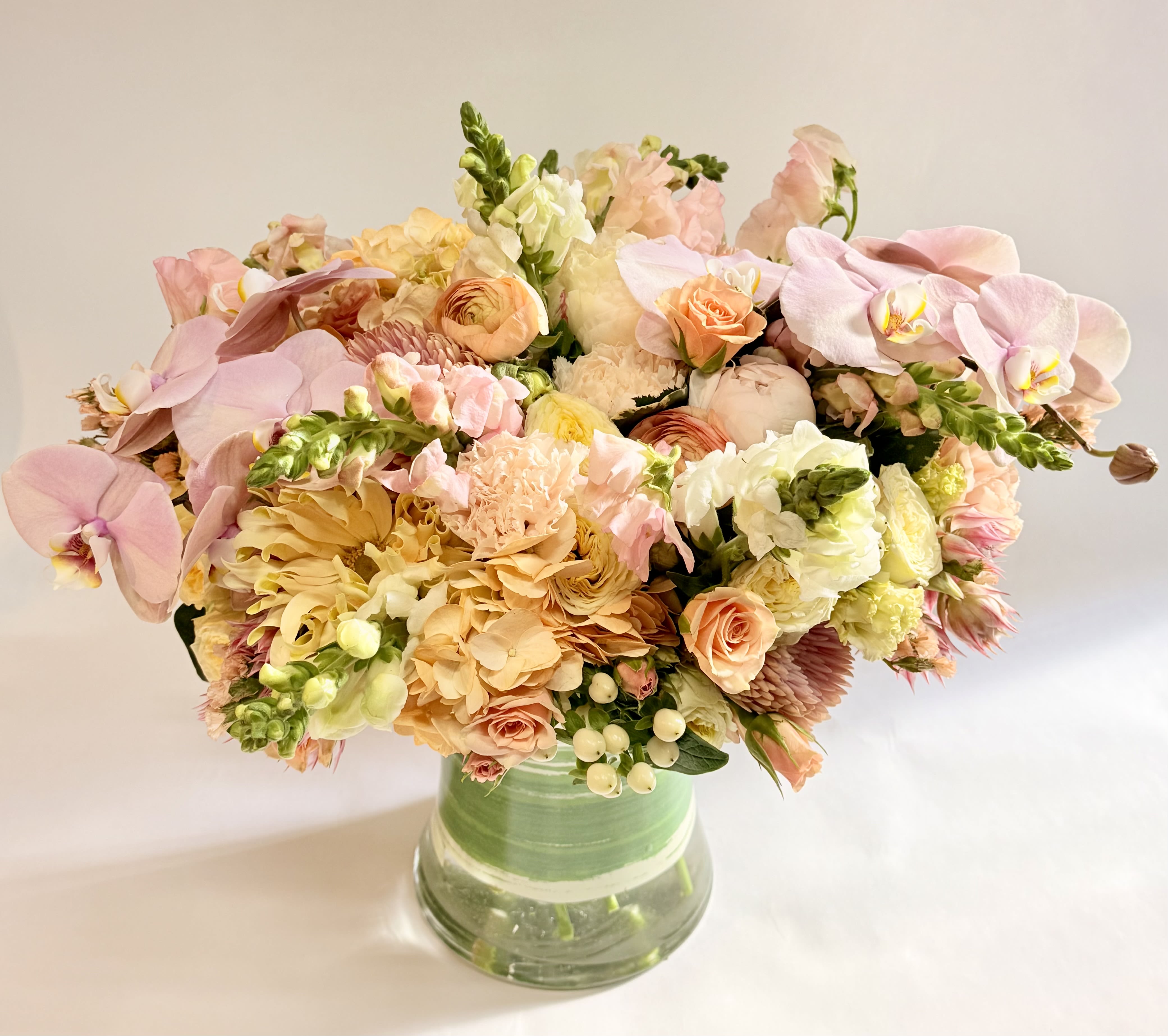 Pastel bouquet of orchids, roses, and mixed blooms in a glass vase