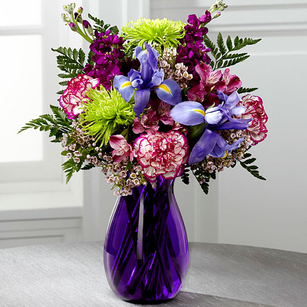 Mixed bouquet of purple, pink, and blue flowers in a purple glass vase