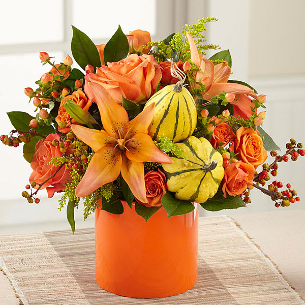 Orange floral arrangement with pumpkins in a bright vase