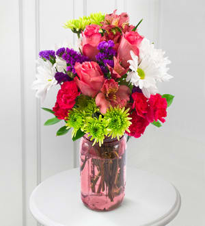 Mixed bouquet of pink roses, white daisies, and purple filler in a pink glass vase