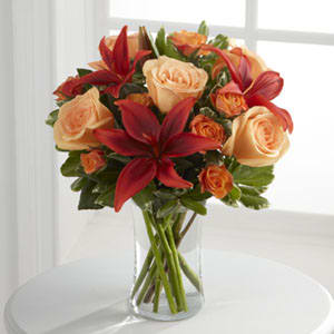 Bouquet of peach roses and red lilies in a clear glass vase