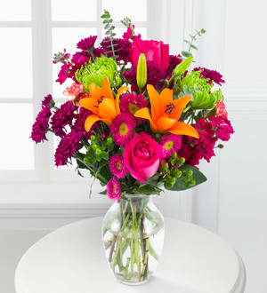 Bouquet of orange lilies, pink roses, and magenta flowers in a glass vase