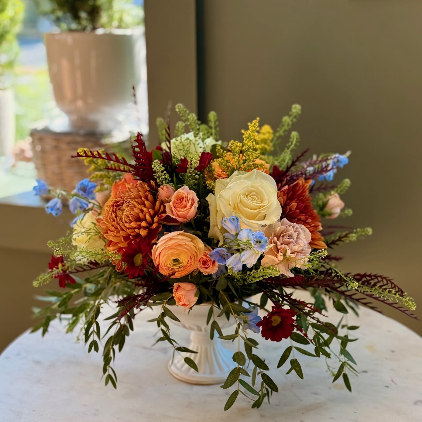 Mixed bouquet in a white pedestal vase with peach, cream, and red blooms