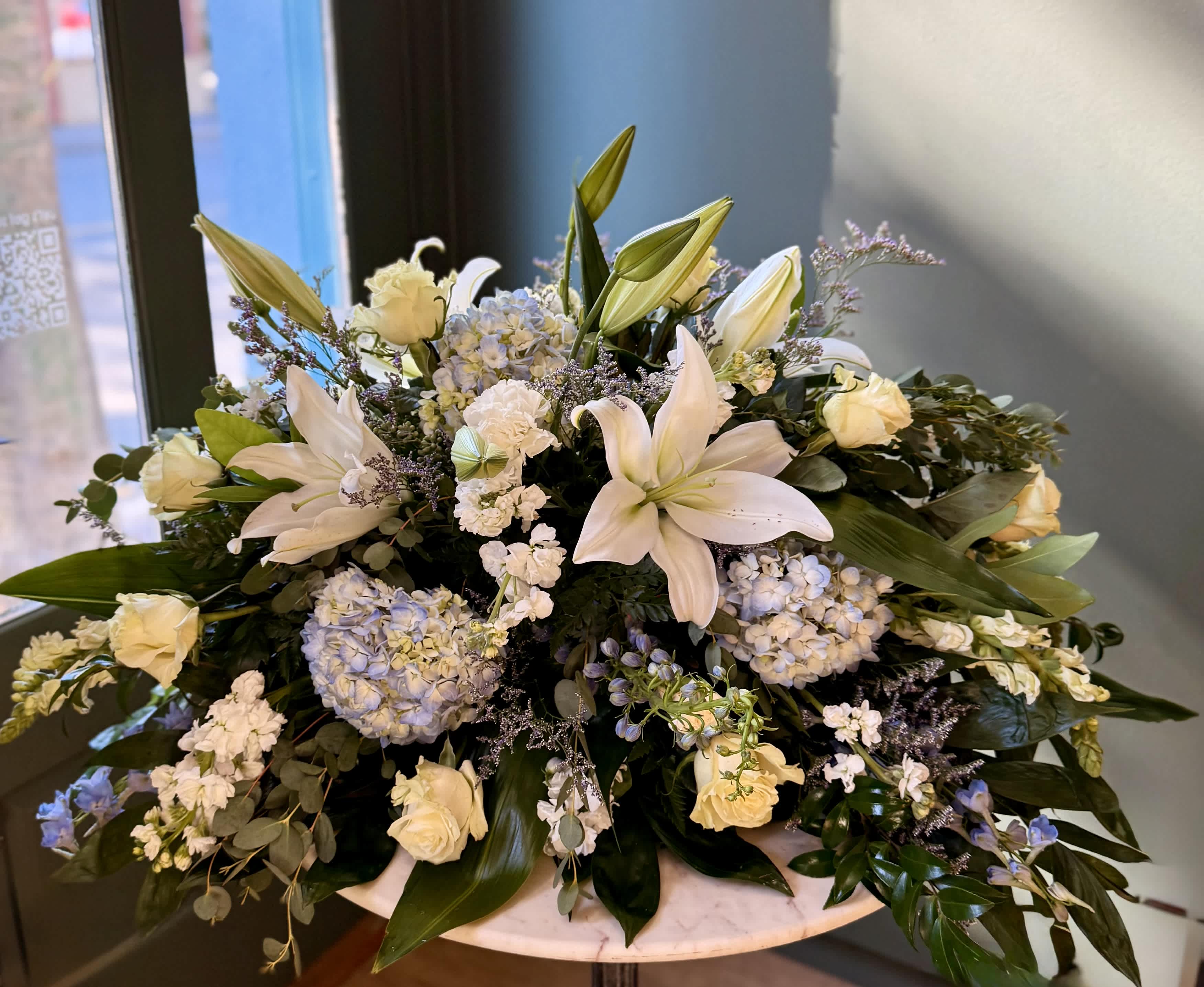 White lilies and pale roses arranged with blue hydrangeas in a low vase