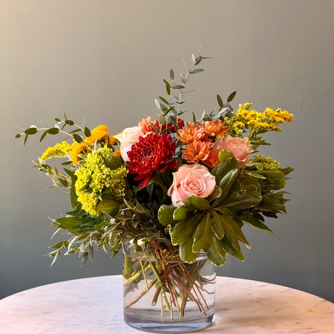 Mixed bouquet of pink, red, and yellow flowers in a clear glass vase