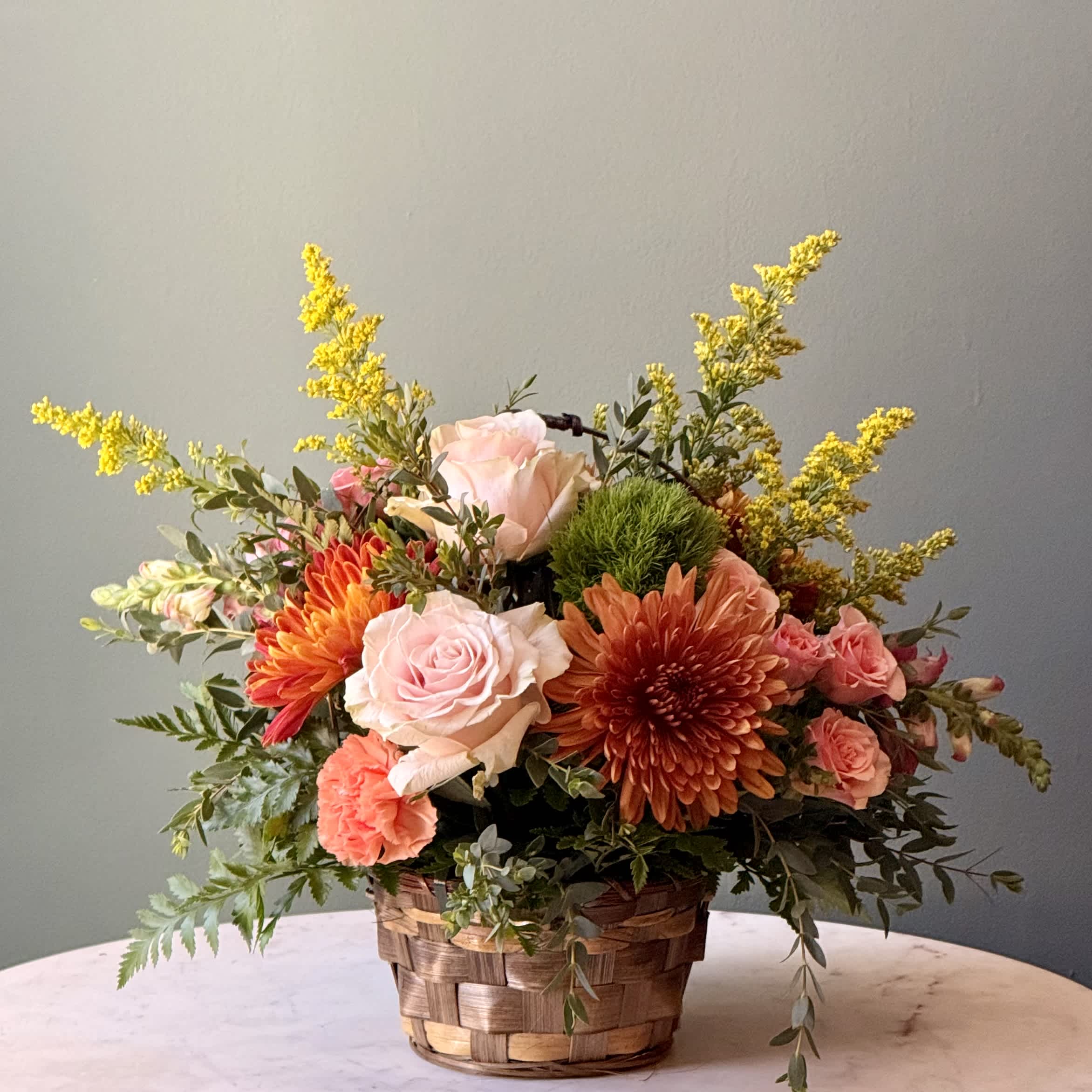 Basket arrangement with pink roses, orange chrysanthemums, and yellow filler flowers