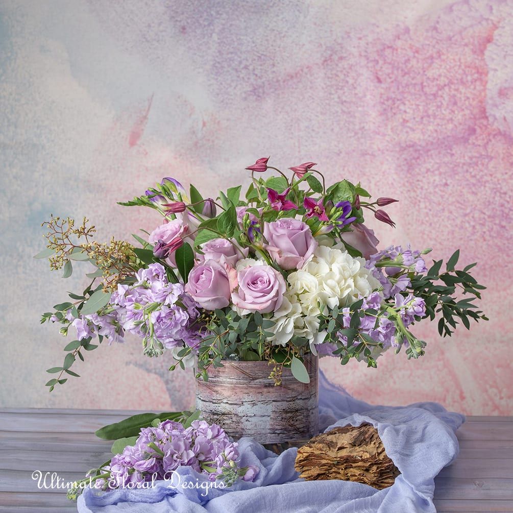 Lavender and white floral arrangement in a rustic container with loose greenery
