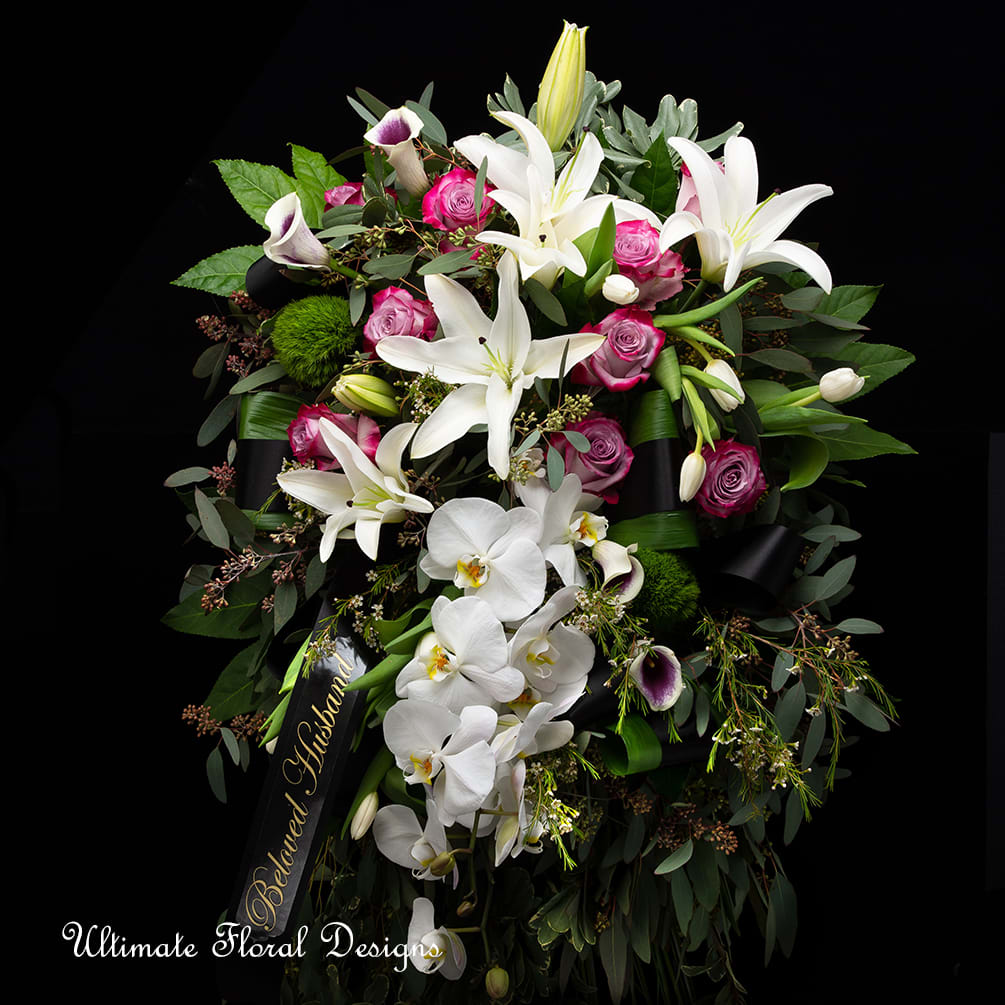 Large funeral spray with white lilies, orchids, and pink roses on a black ribbon