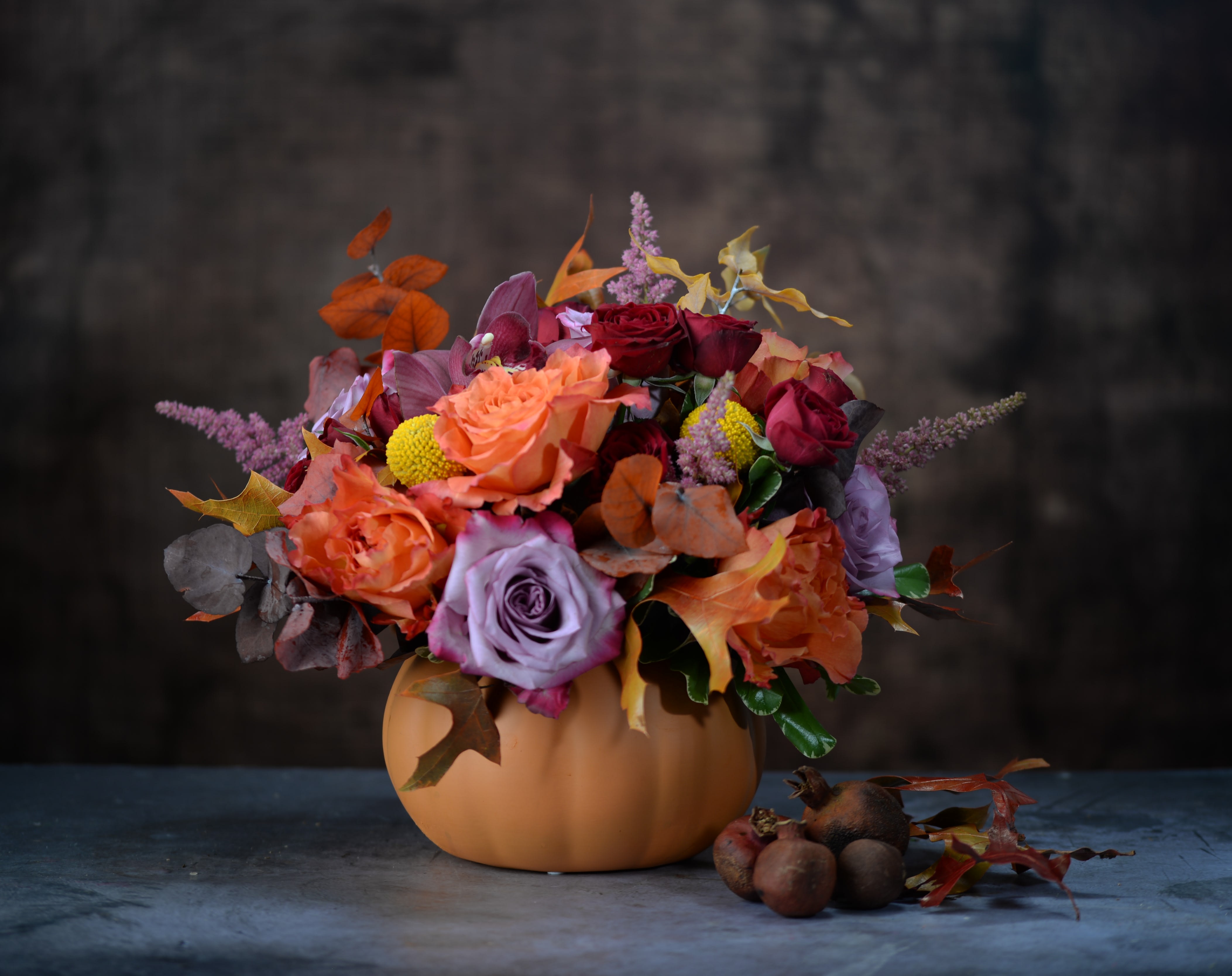 Autumn bouquet in a pumpkin-shaped vase with roses and mixed blooms