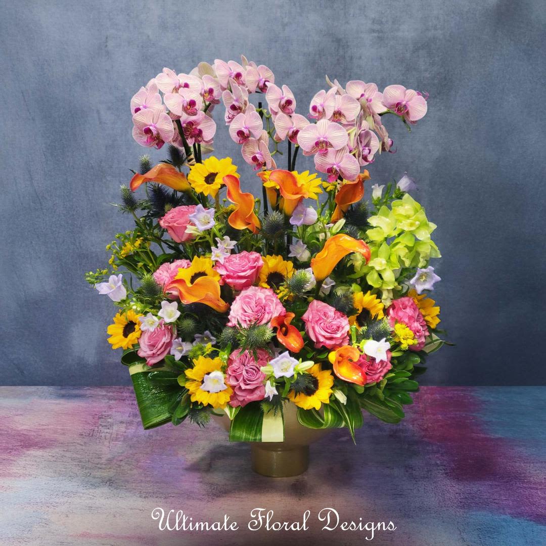 Mixed floral arrangement with pink orchids, roses, calla lilies, and sunflowers in a vase