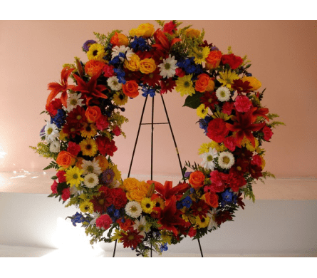 colorful Sympathy Wreath -  W519 - Here is a colorful sympathy and funeral wreath made with a variety of different color Roses Tiger Lilies Mums Asters Bella Donna Carnations and Solidasters. This beautiful standing wreath arrangement comes with a five foot easel and is appropriate for large corporate events funeral services and any other mass event.Dimensions Approximately: 22" H x 22" W As Shown : W519