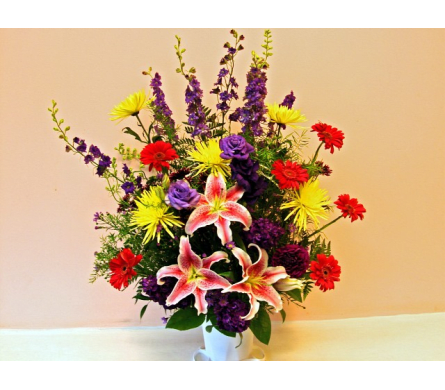Colorful bouquet with pink lilies, purple flowers, and red and yellow daisies in a white vase
