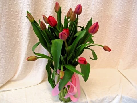 Bouquet of red and pink tulips in a clear glass vase with a pink ribbon