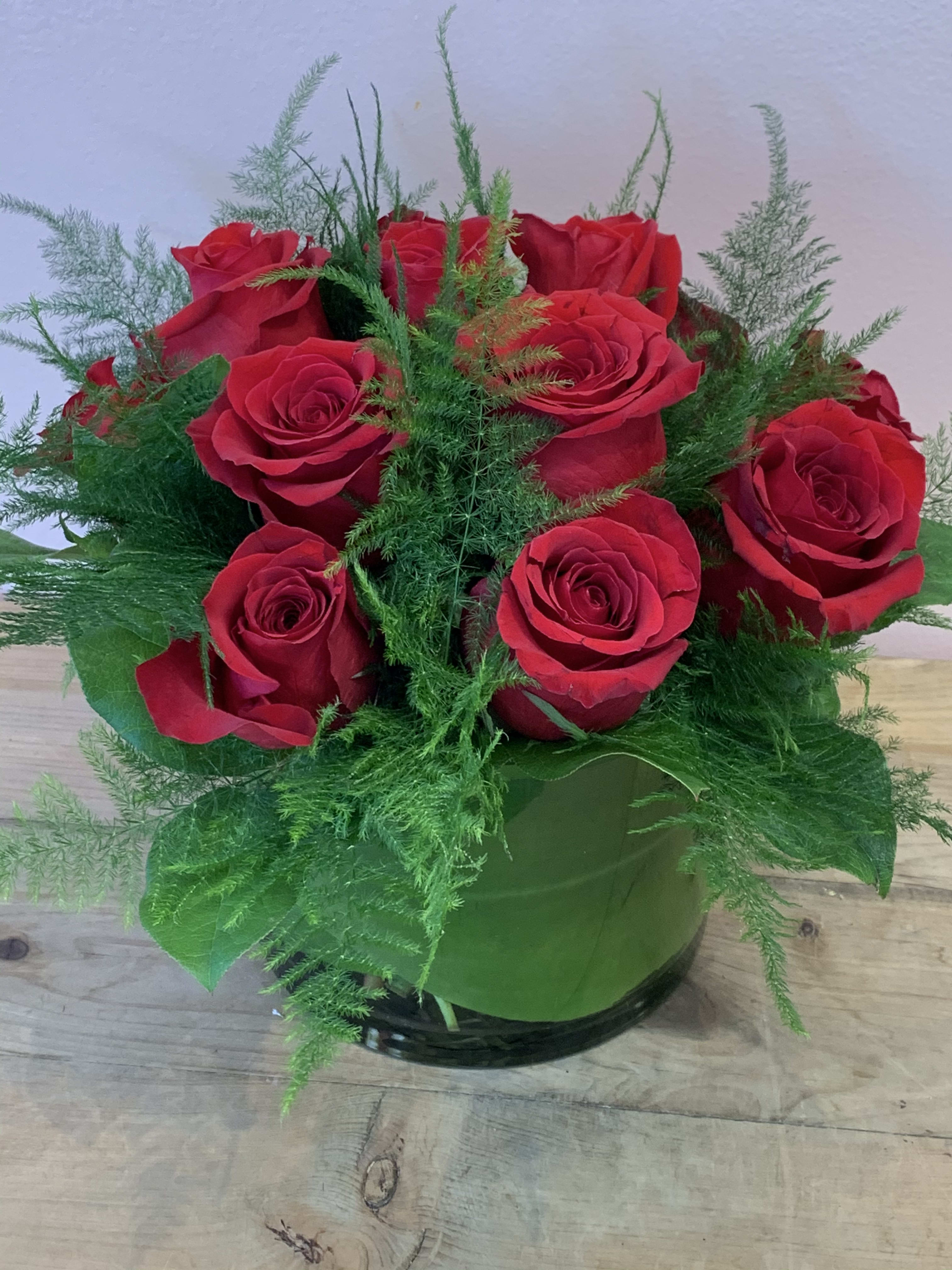 Red roses arranged in a round glass vase with airy greenery