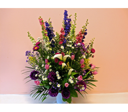 Honorary Floral Arrangement - W207 - An outstanding floral spray designed with the colors of purple white pink and blue. Honorary Floral Arrangement is an exceptional spray for funeral and or sympathy services. Honorary Floral Arrangement is a large one sided flower spray made with Calla Lilies Larkspurs Dahlias Tulips Asters Solid Asters and white Monte Casino Aster.Dimensions Approximately: 25" H x 12" W As Shown : W207