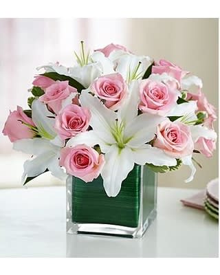 Pink roses and white lilies arranged in a clear square vase