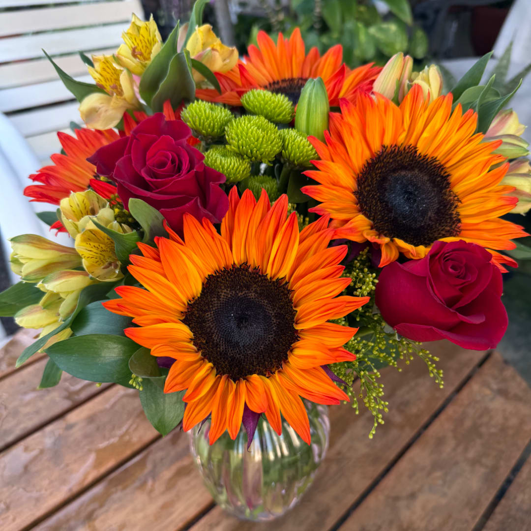 Bouquet of orange sunflowers, red roses, and yellow alstroemeria in a glass vase