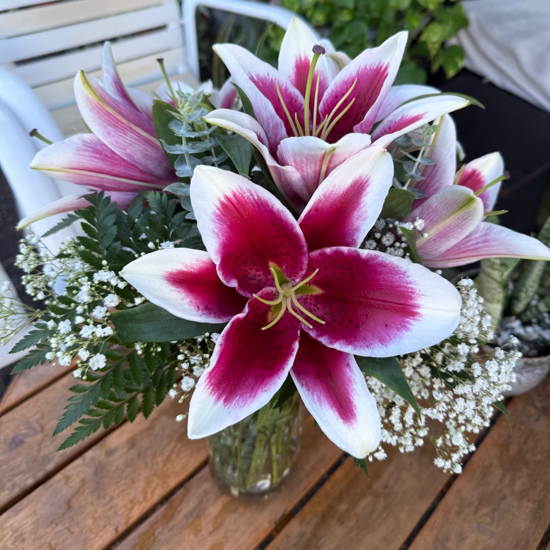 Pink and white lilies arranged in a glass vase with baby's breath