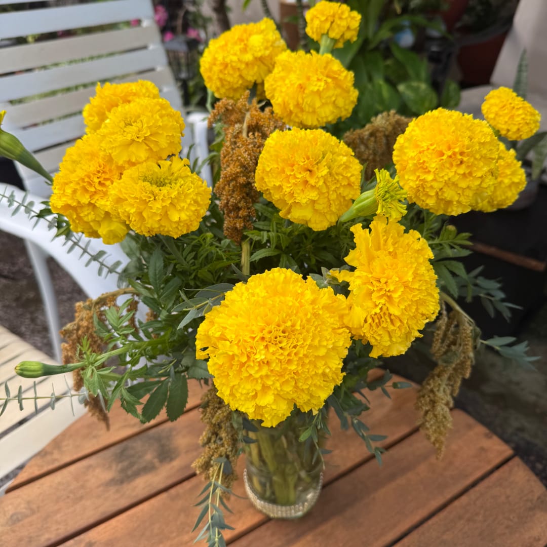 Yellow marigold bouquet in a clear glass vase on a wooden table