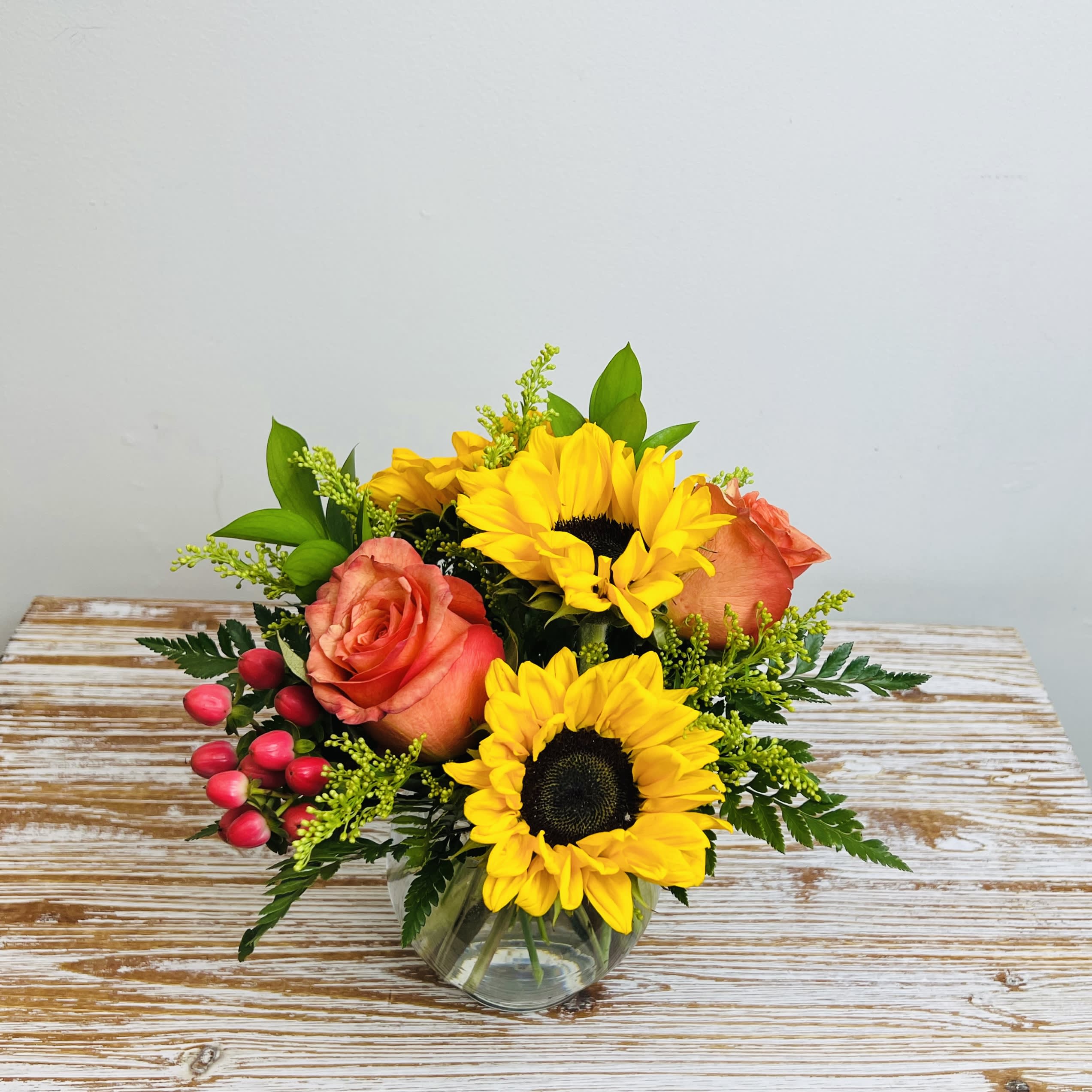 Sunflowers and orange roses in a clear glass vase