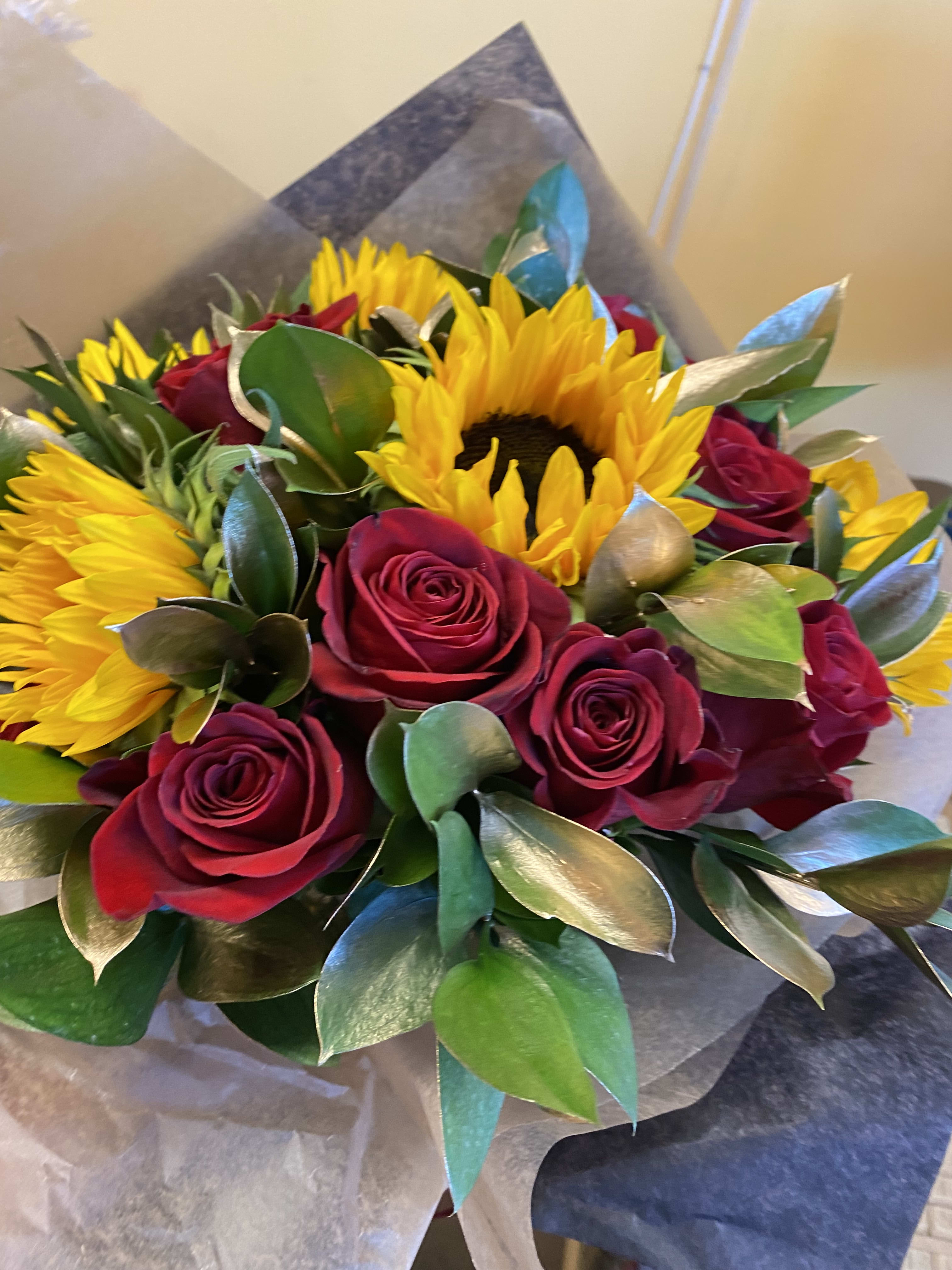 Bouquet of red roses and yellow sunflowers wrapped in paper