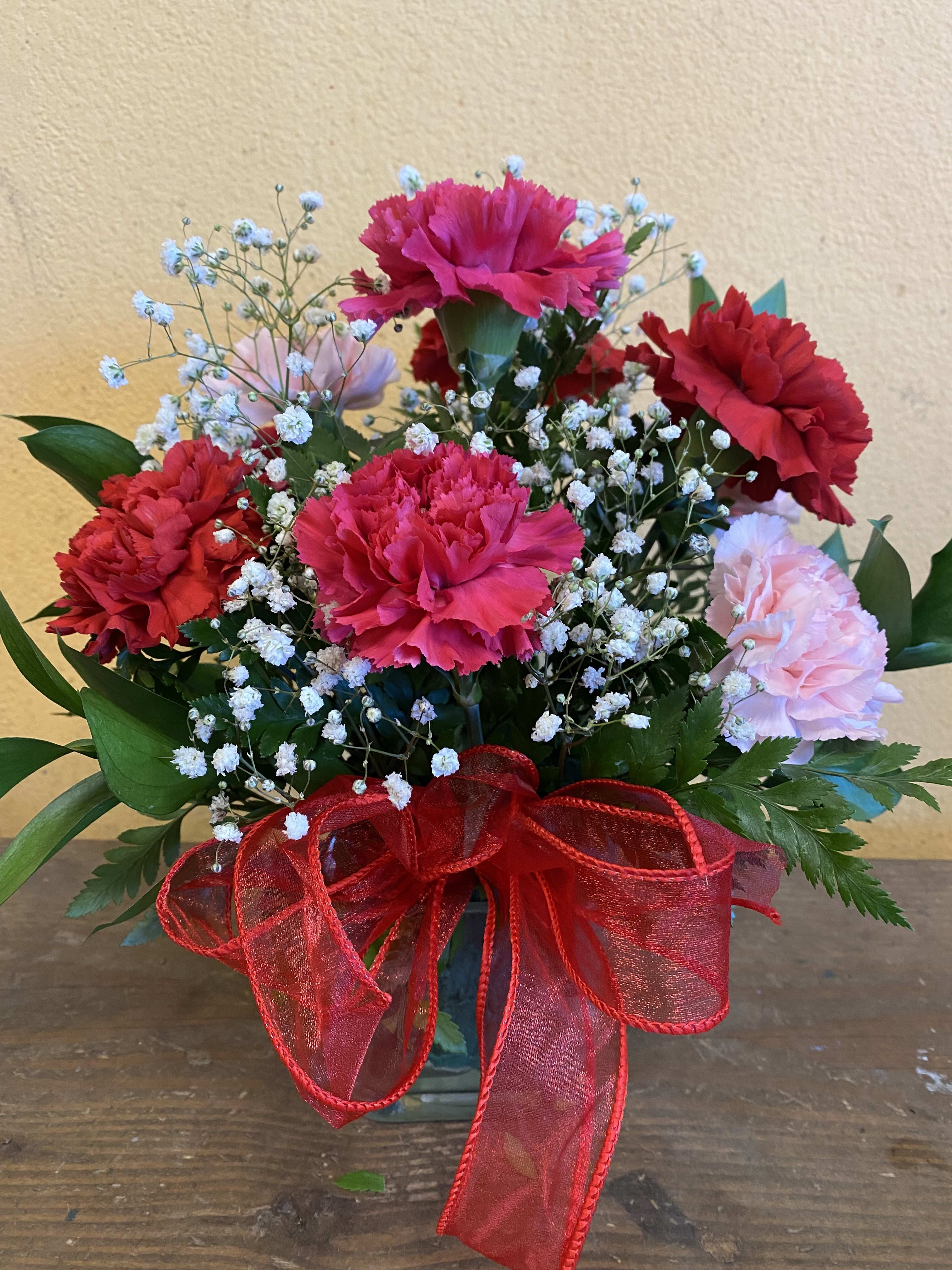 Carnation bouquet in a glass vase with red ribbon