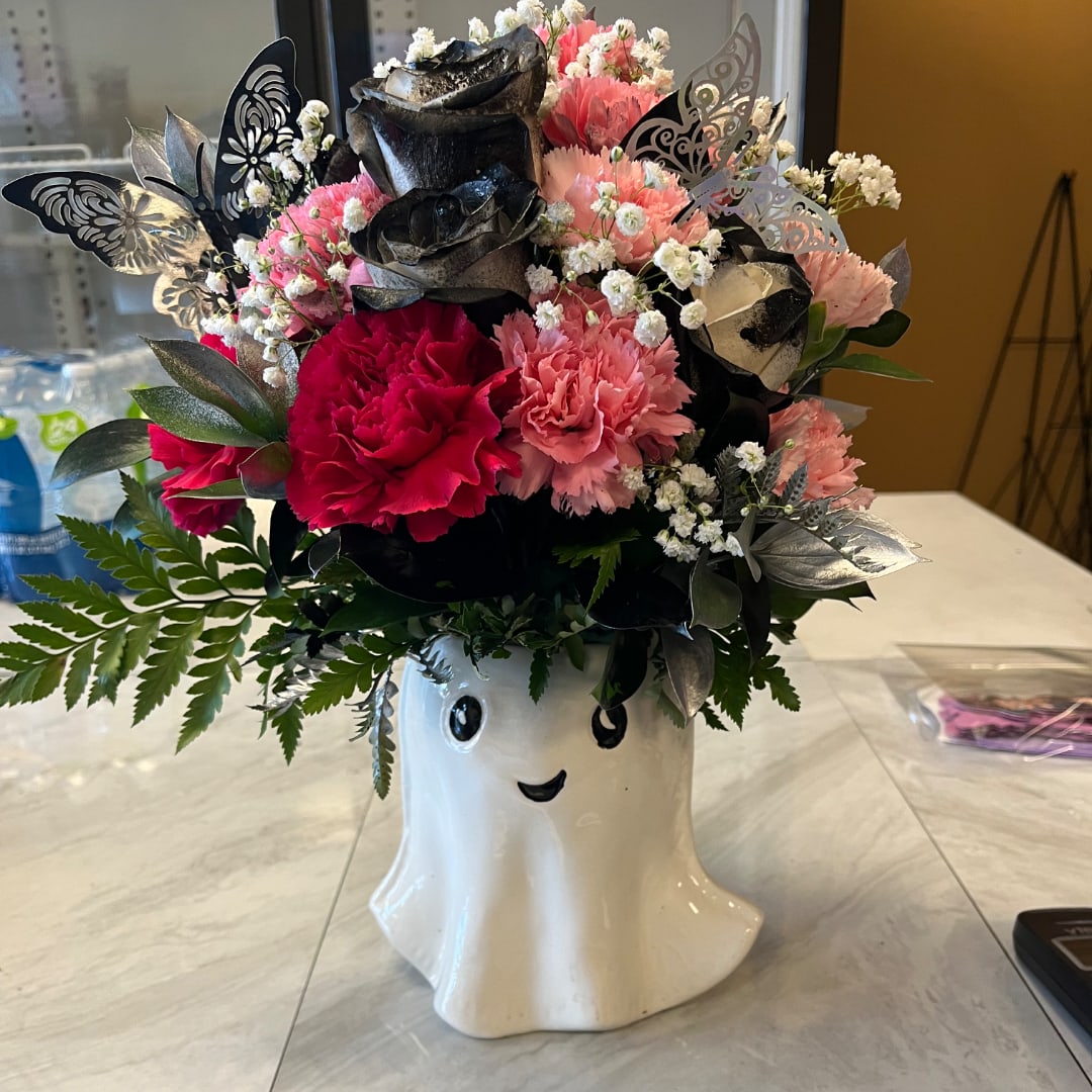 Pink and black floral arrangement in a ghost-shaped vase with butterfly accents