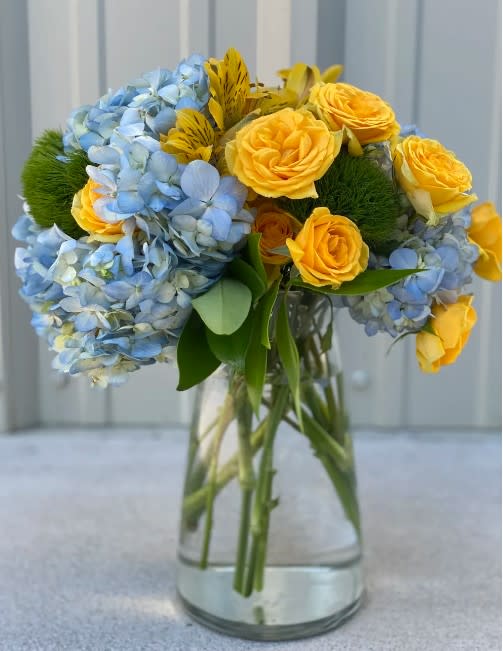 Bouquet of blue hydrangeas and yellow roses in a clear glass vase