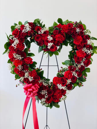 Heart-shaped red rose wreath on a stand with a pink ribbon bow