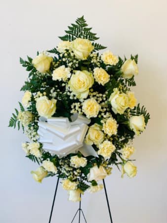 White floral funeral wreath on a stand with a ribbon bow