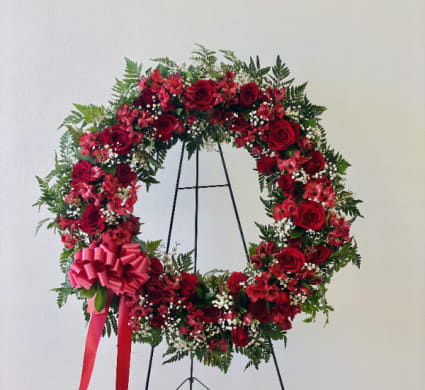 Red rose wreath on a black stand with a pink bow
