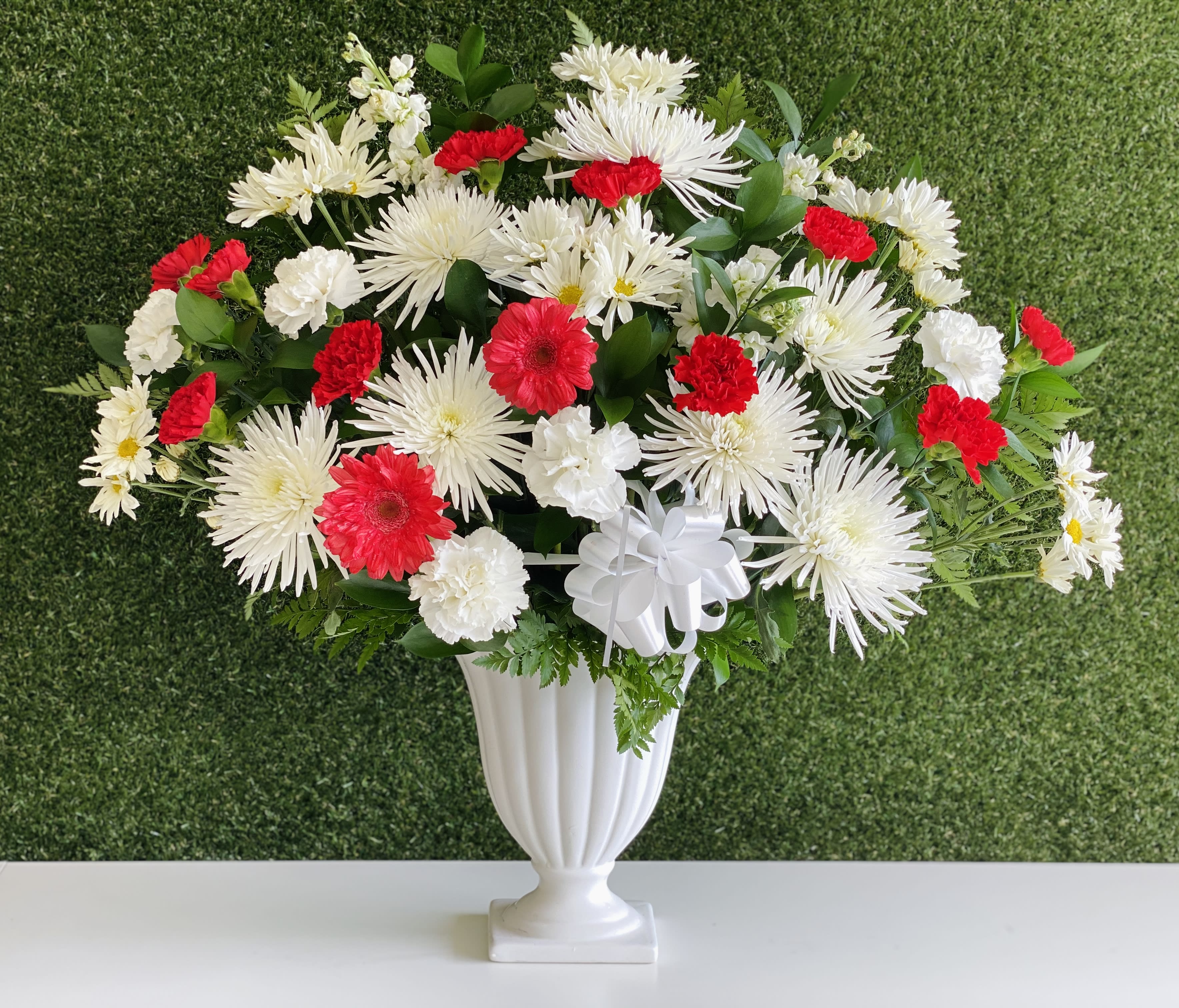 White and red floral arrangement in a white urn vase