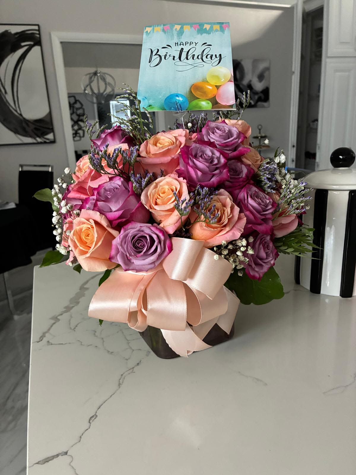 Bouquet of pink, peach, and lavender roses with a birthday card and ribbon