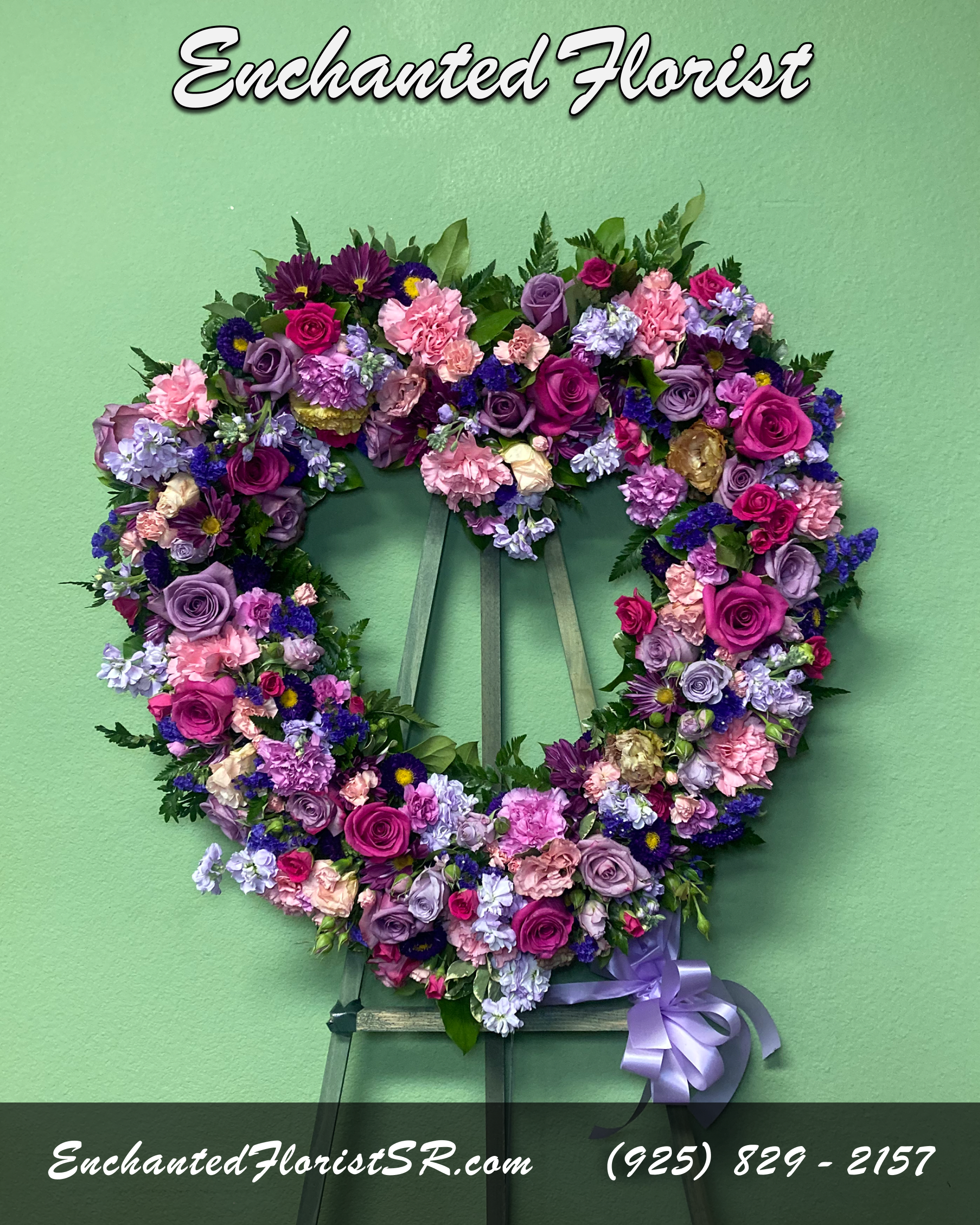 Lavender Tribute - Standing Wreath  - Lavender Tribute is a tranquil Standing Wreath of flowers that arrives delivered on an easel, showcasing a heart-shaped wreath covered in an array of lavender flowers, featuring pink, purple and lavender Roses, Carnations, Stock, Chrysanthemums, Asters and Statice, accented with lush, verdant Leather Fern.  Crafted with care, Lavender Tribute stands as a beautiful reflection of the life and love shared. Whether adorning a memorial service or providing solace in a time of loss, this arrangement conveys deep sentiment and honors the legacy of a loved one in a way that words often cannot.  Arrives In: 1 wooden easel  Orientation: One-Sided  Approximate Dimensions: Height: 24" Width: 24"