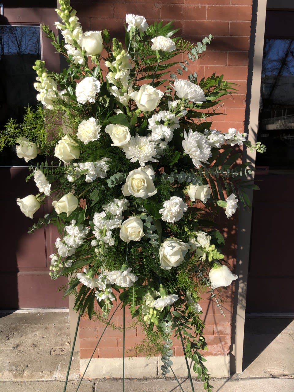 Tall standing spray of white roses, carnations, and other flowers on a metal easel