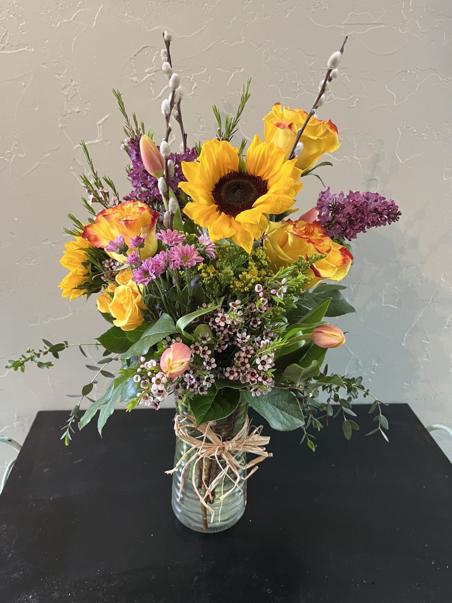 Bouquet of sunflowers, yellow roses, and purple flowers in a glass vase