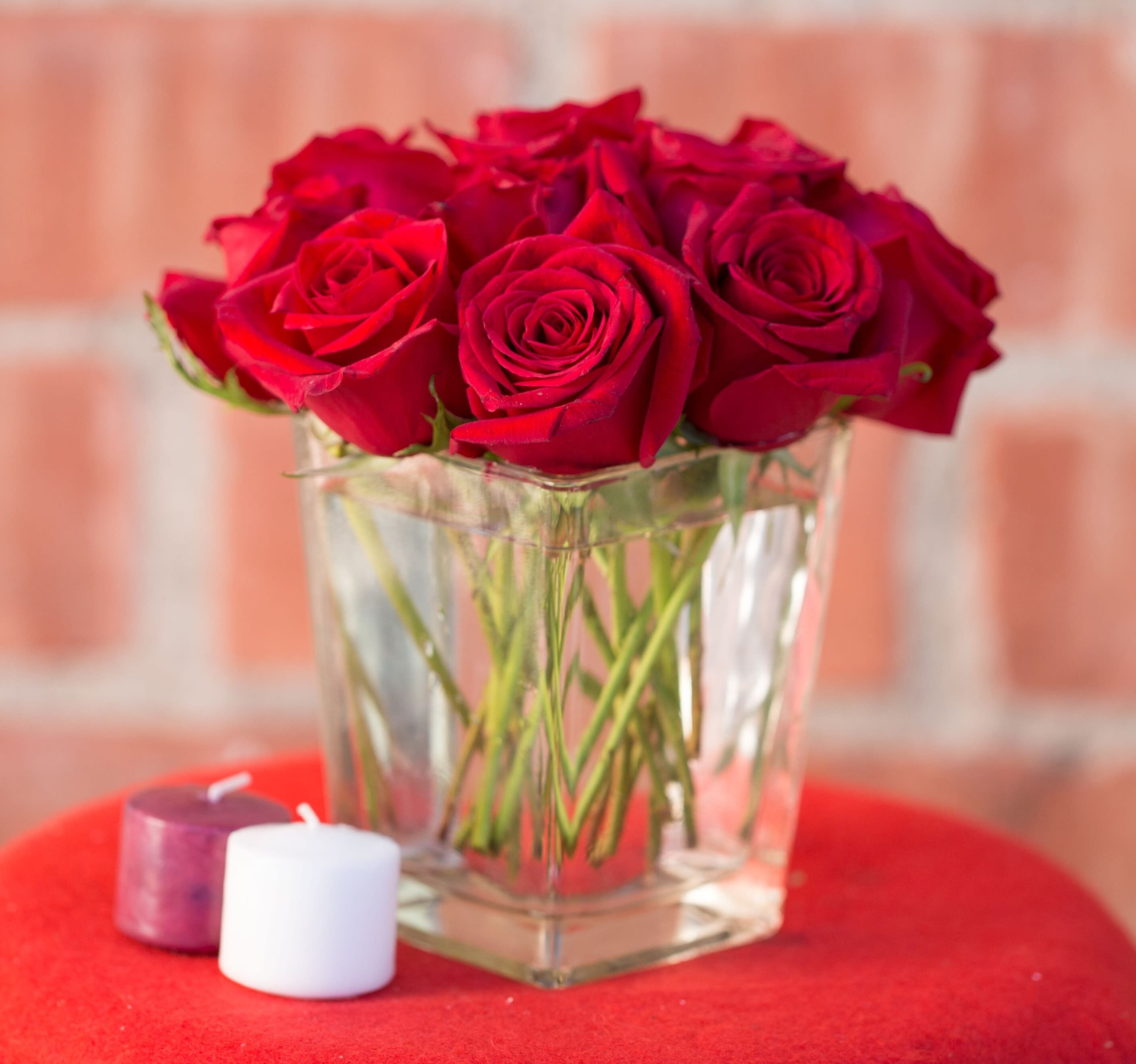 Red roses in a clear glass vase with two small candles nearby