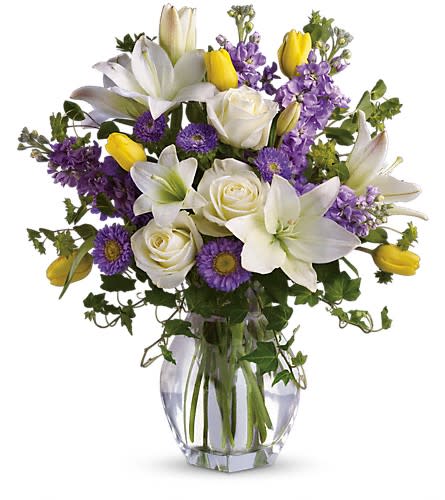 Bouquet of white lilies, roses, and purple flowers in a glass vase