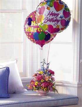Birthday balloons above a pink flower arrangement in a vase