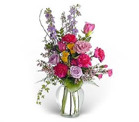 Mixed bouquet of pink, purple, and yellow flowers in a clear glass vase