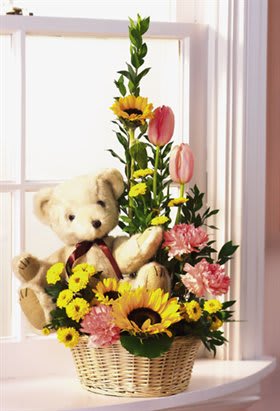 Teddy bear in a basket with sunflowers, tulips, and pink flowers
